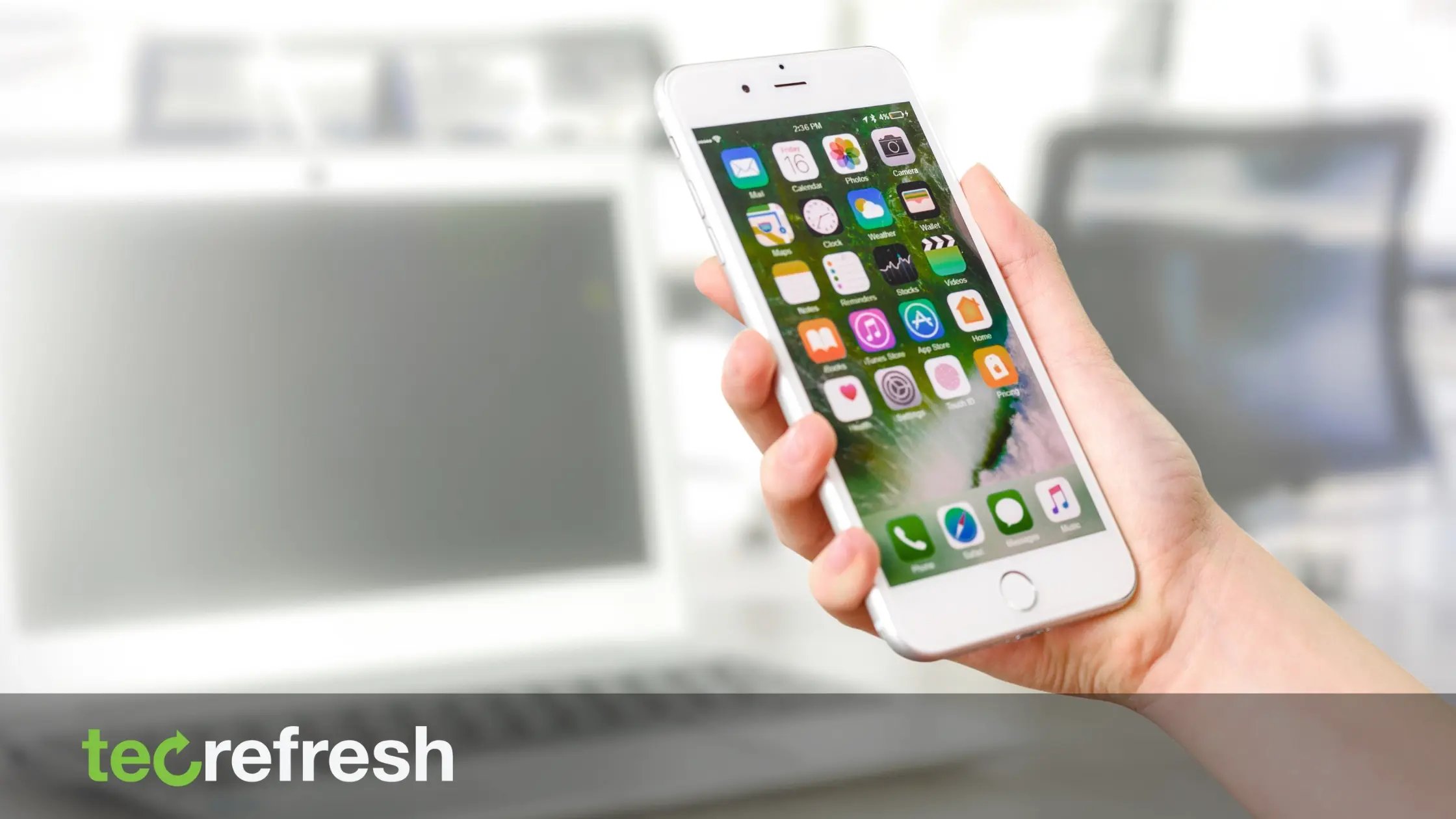 Hand holding iPhone displaying app icons with blurred laptop in the background - mobile device management concept