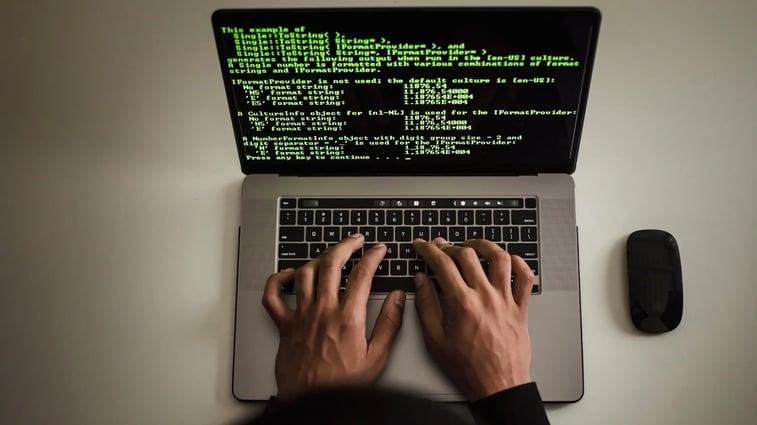 Close-up of hands typing on a laptop with green code on screen, representing software development, programming, or ethical hacking