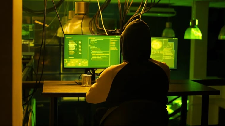 Hacker working on multiple computer monitors displaying code, symbolizing cybersecurity threats and the importance of securing data in a digital world.